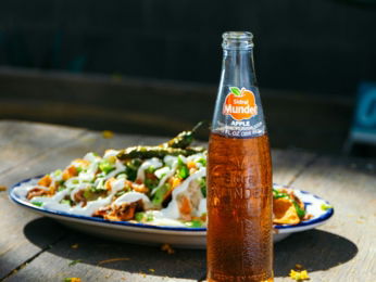 a bottle of soda sitting on top of a table next to a plate of food